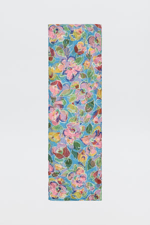 The Julien - Jeannie Bloom Sky is a rectangular yoga mat showcasing a vibrant floral pattern with pink, yellow, and blue flowers plus green leaves on a light, multicolored background.