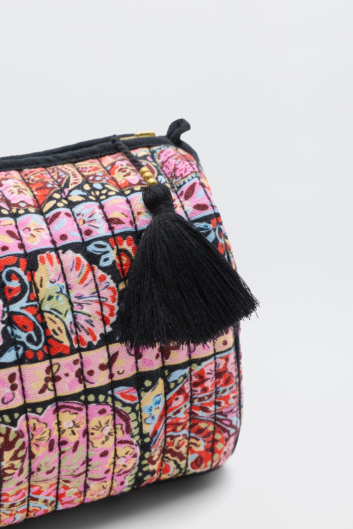 The Jadina - Cara Stripe Black is a colorful quilted pouch with a butterfly pattern and a large black tassel on the zipper, pictured on a plain white background.