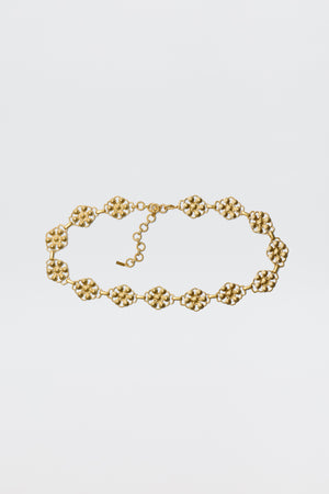 The Tiana - Gold necklace showcases vintage-gold plating with linked, textured floral motifs and an adjustable chain clasp, styled like a daisy-chain belt and displayed against a plain white background.