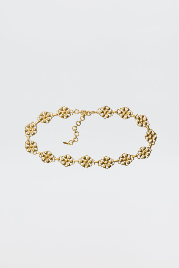 The Tiana - Gold necklace showcases vintage-gold plating with linked, textured floral motifs and an adjustable chain clasp, styled like a daisy-chain belt and displayed against a plain white background.