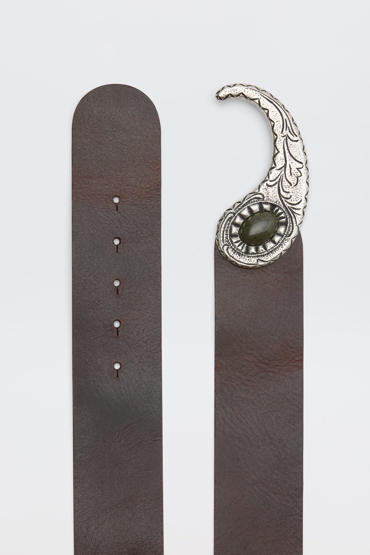 The Daniella - Dark Brown is a brown leather belt with a decorative silver buckle featuring an ornate curved design and a dark oval stone in the center, shown laid flat with both ends visible.