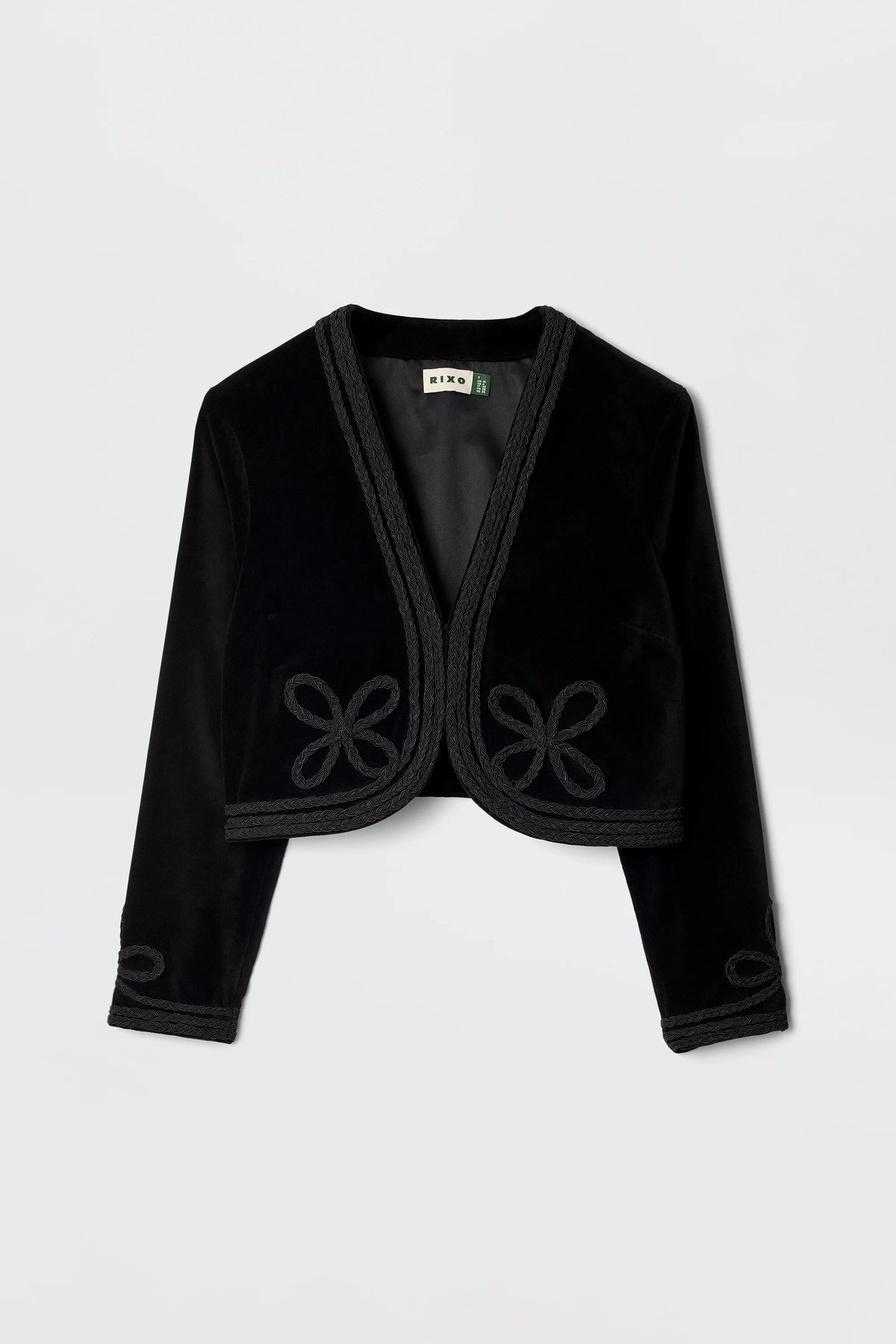 The Kesia - Clover Appliqué Black is a vintage-inspired cropped black velvet jacket featuring long sleeves, decorative trim, and knotted detailing on the front and cuffs, shown against a plain white background.