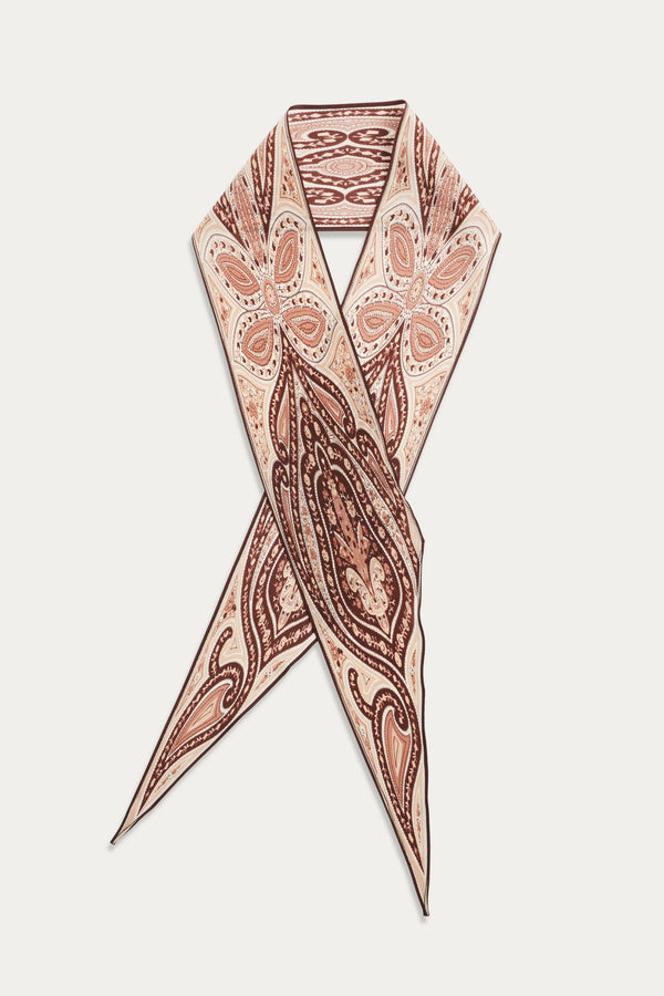 The Yelina - Paisley Flora Brown scarf is made of silk and showcases brown and peach paisley floral patterns on a beige background, arranged in a crisscrossed, pointed design against white.