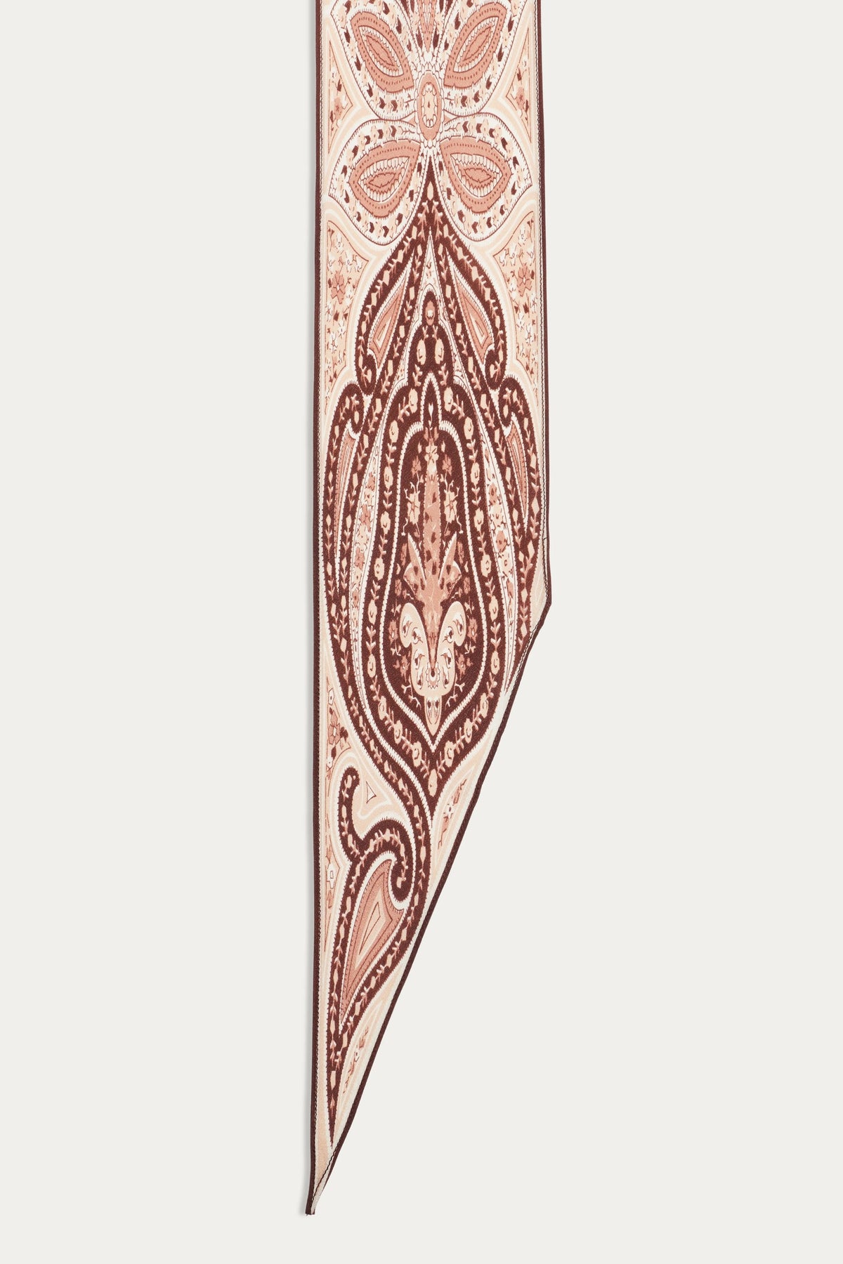 A close-up of the Yelina - Paisley Flora Brown scarf reveals an intricate paisley and floral print in brown, pink, and cream on a white background, finished with a pointed asymmetrical edge.