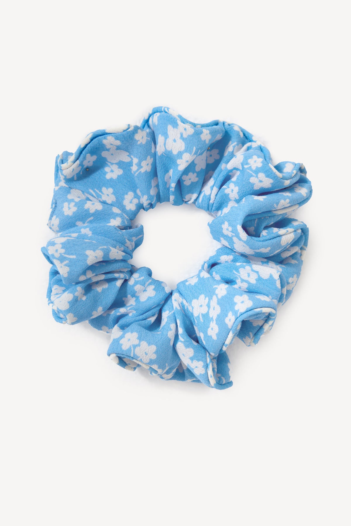 The Jasper - Violet Ditsy Blue scrunchie is a chunky blue fabric accessory with a white floral pattern, shown on a plain white background.