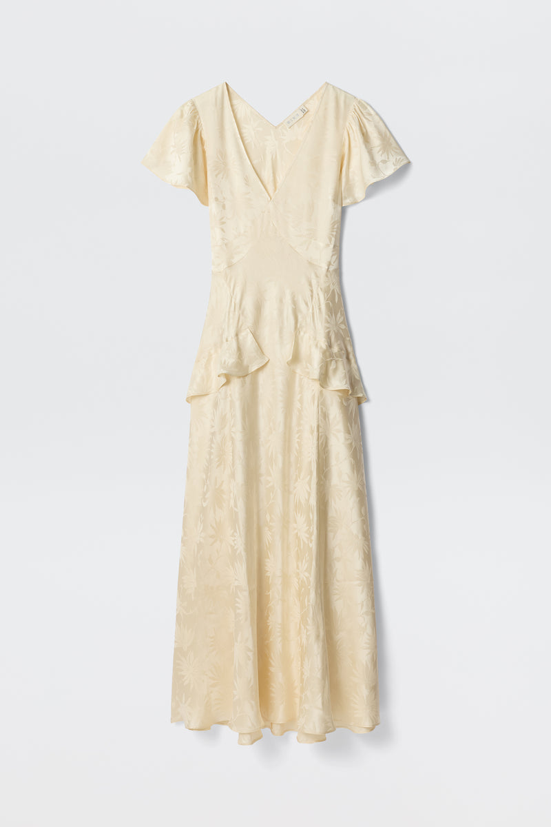 The Evie - Daisy Jacquard Champagne is a cream midi dress in silk-jacquard, featuring short sleeves, a V-neckline, subtle floral pattern, and waist ruffles—elegantly showcased against a plain white background.