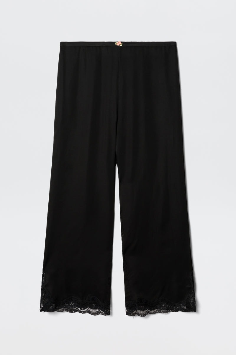 The Mireille - Black satin pajama pants feature a relaxed fit, lace-trimmed hem, and a small decorative bow at the waistband, shown against a plain white background.