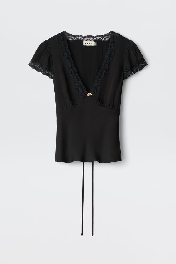 The Karia - Black blouse features short sleeves, lace trim on the V-neck and sleeves, a central decorative button, and two long waist ties.