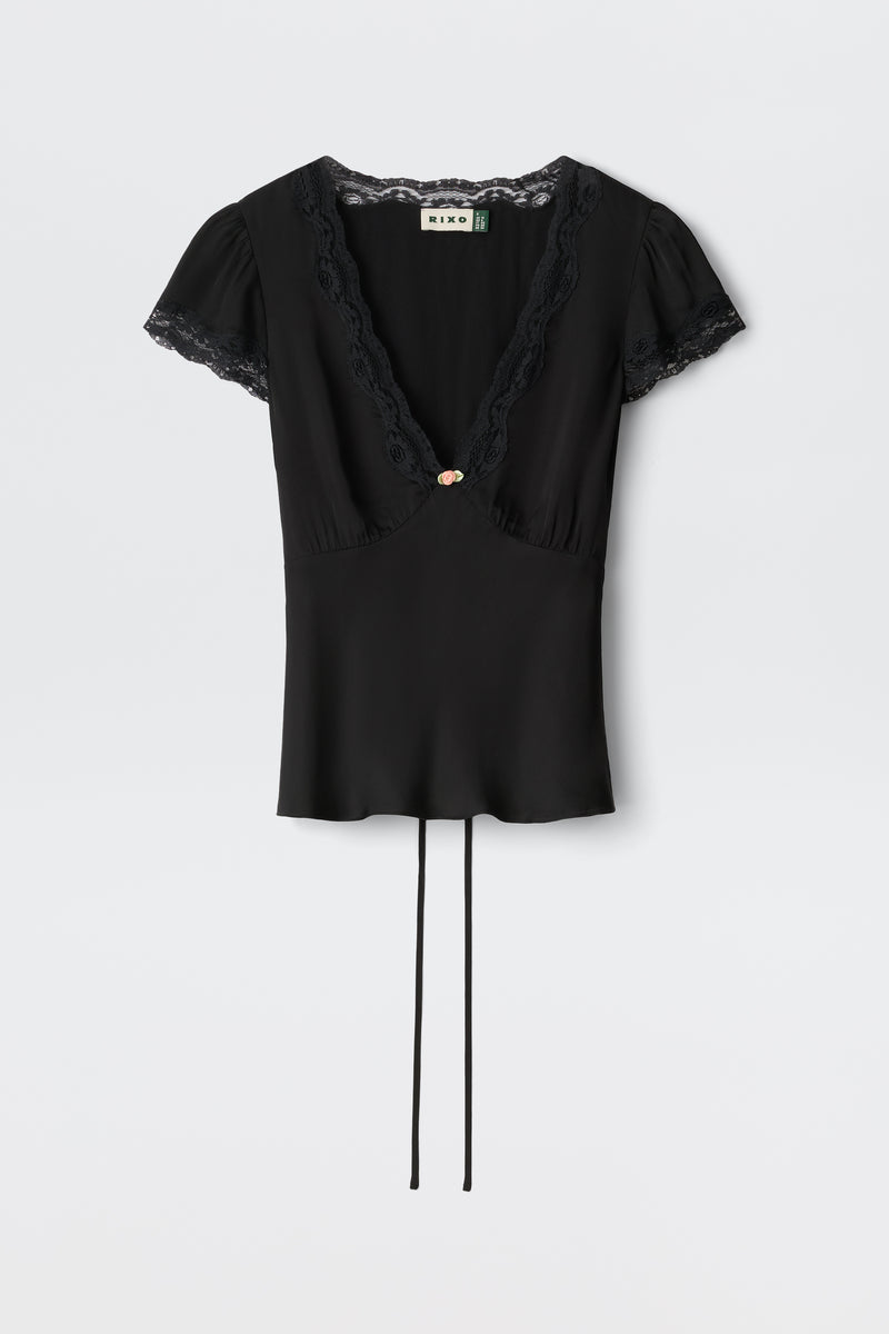 The Karia - Black blouse features short sleeves, lace trim on the V-neck and sleeves, a central decorative button, and two long waist ties.
