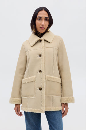 A woman wears the Ellis - Cream faux-shearling coat with front pockets and button closures, styled with blue jeans against a light background—ideal autumn outerwear.