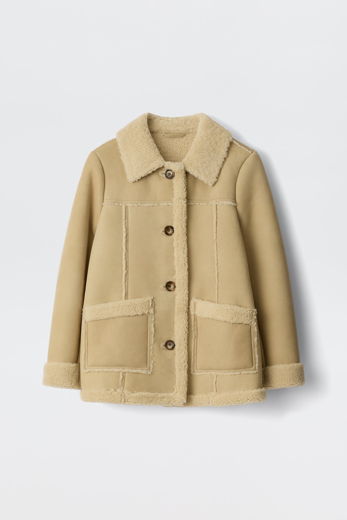 The Ellis - Cream is a tan faux-shearling jacket with a wide collar, button front, large patch pockets, and visible cream lining on the edges—an ideal choice for autumn outerwear, shown against a white background.