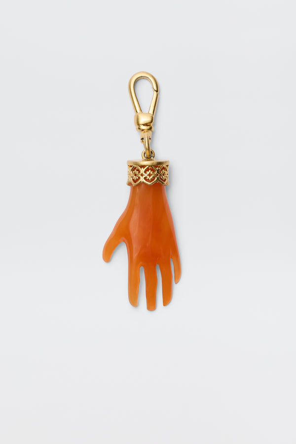 The Hand - Orange keychain features an orange, gold-plated hand charm with a gold ornate band at the wrist, attached to a gold lobster clasp. Shown against a plain white background.