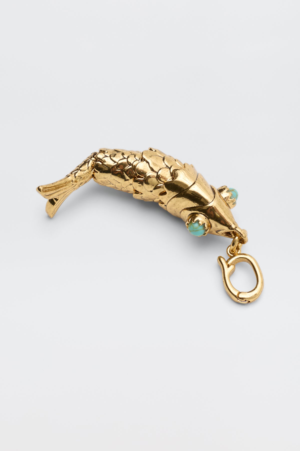 Nerissa - Gold: A gold, fish-shaped pendant featuring detailed scales, turquoise eyes, and a clasp at the mouth, shown against a plain light background.