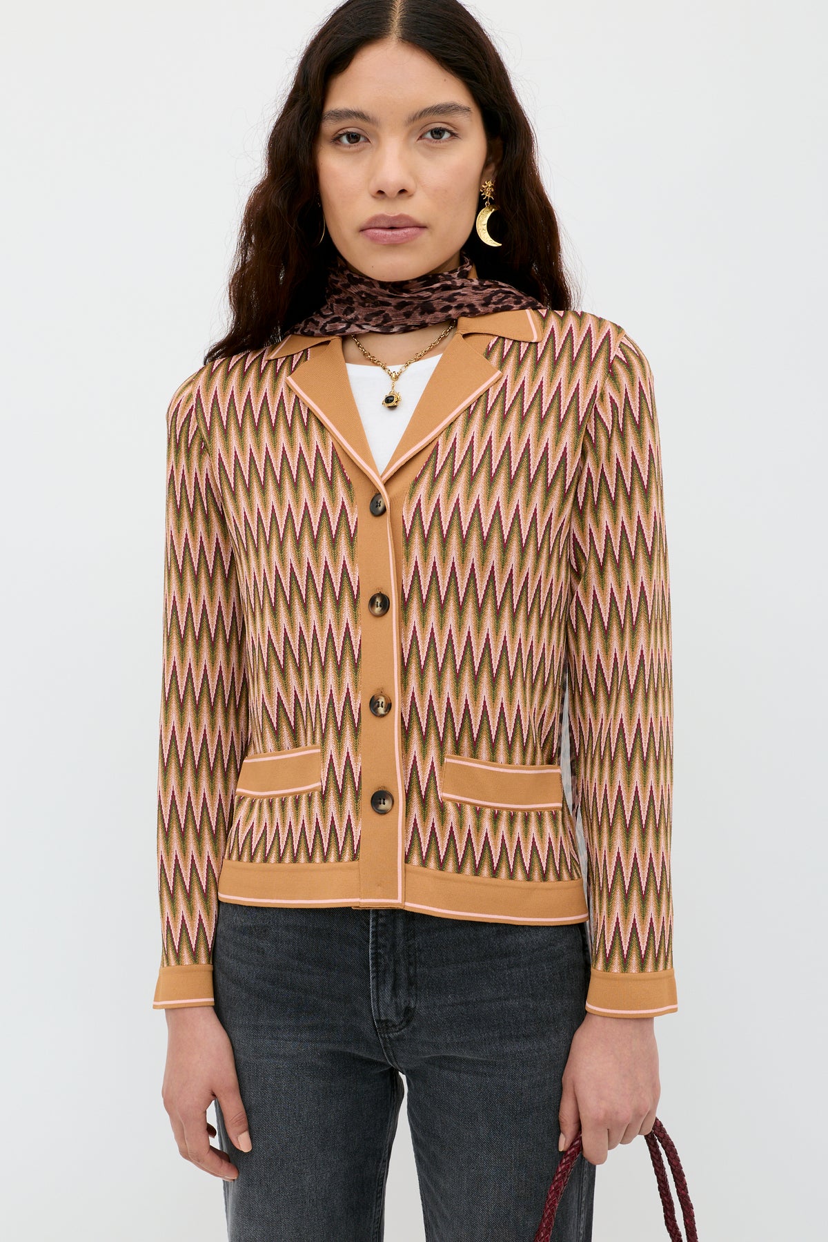 A woman wears the Quinley - Maeve Jacquard Multi cardigan over a white top with dark jeans, gold earrings, layered necklaces, and a brown scarf, standing against a plain white background.