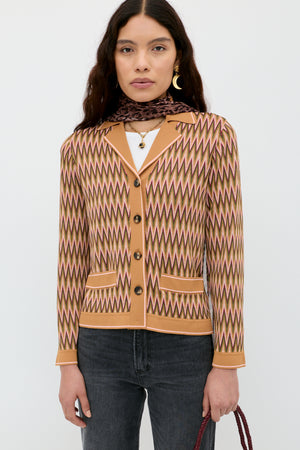 A woman wears the Quinley - Maeve Jacquard Multi cardigan over a white top with dark jeans, gold earrings, layered necklaces, and a brown scarf, standing against a plain white background.