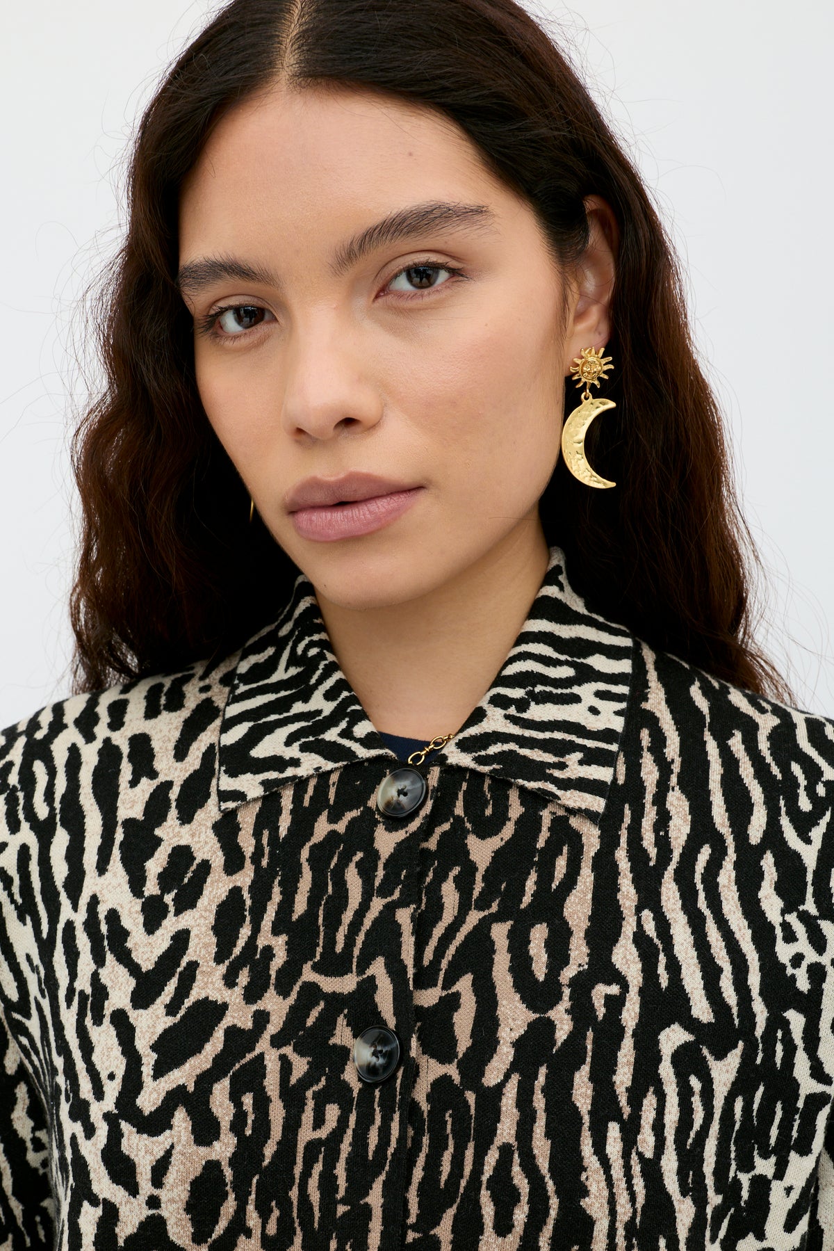 A woman with long, wavy brown hair wears the Trista - Bohemia Leopard Brown jacket and gold sun and crescent moon earrings, looking directly at the camera with a neutral expression.