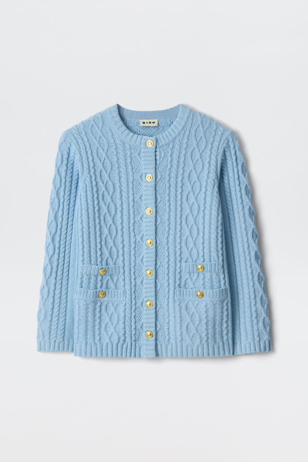 Maurya - Dusty Blue: A cable-knit cardigan in dusty blue with a round neckline, long sleeves, gold front buttons, and two small front pockets, shown against a plain white background.