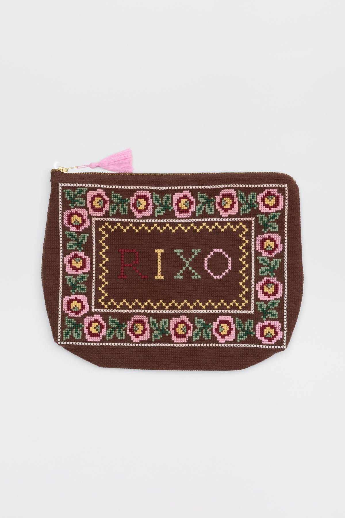 A brown Reiko Rosalia pouch with a floral border, featuring the word “RIXO” cross-stitched in colorful thread at the center and finished with a pink tassel on the zipper.