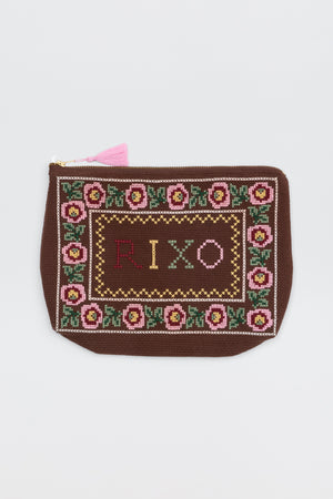 A brown Reiko Rosalia pouch with a floral border, featuring the word “RIXO” cross-stitched in colorful thread at the center and finished with a pink tassel on the zipper.