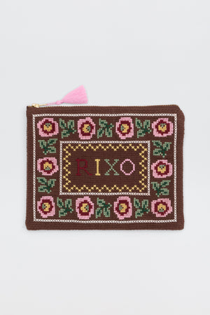 The Beau - Rosalia Cross Stitch Embroidery Brown is a rectangular brown zip pouch with a pink tassel, pink and green floral embroidery along the border, and "RIXO" stitched in the center.