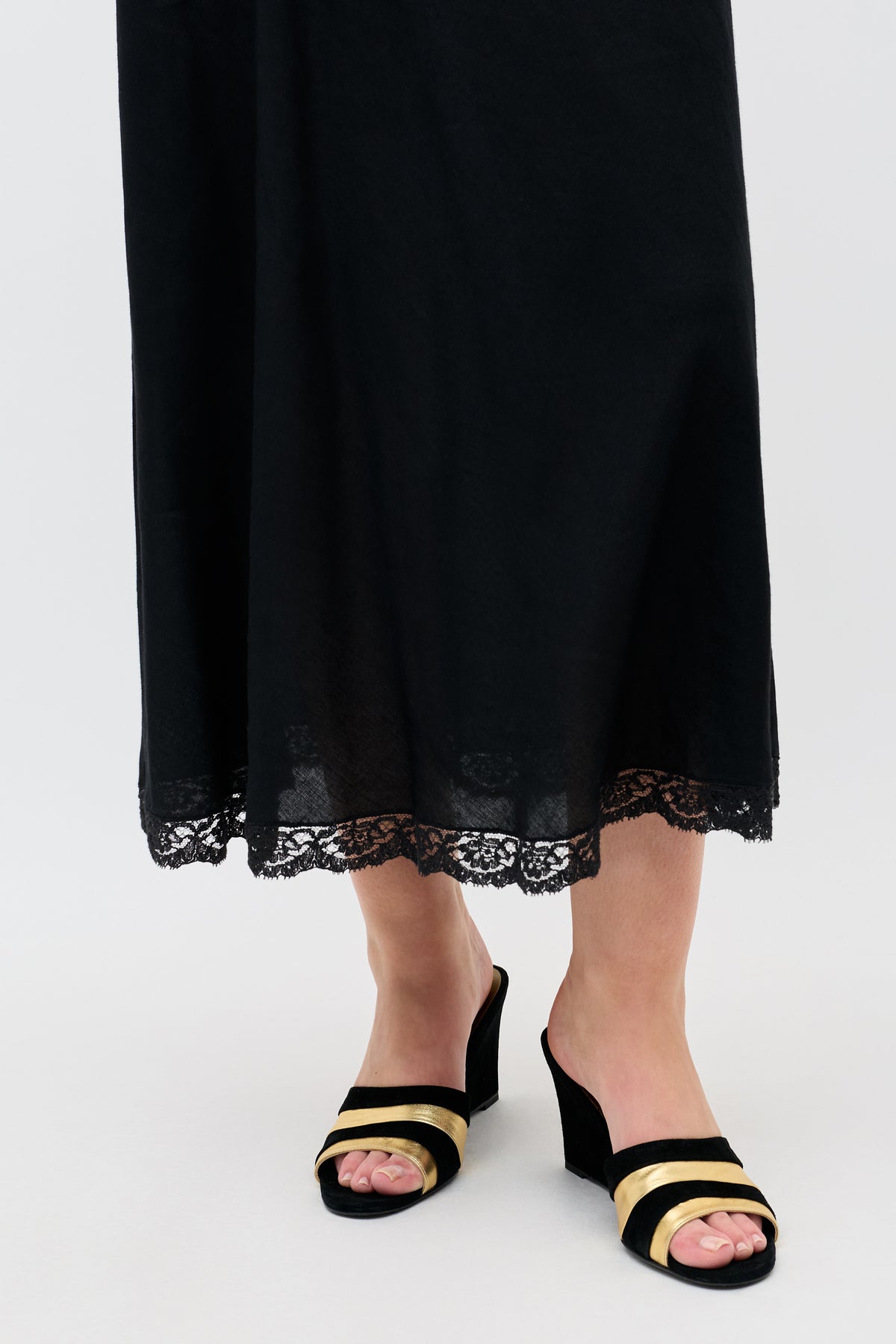 Wearing a long black skirt with lace trim and ’70s-inspired Alira - Gold wedges, a person stands on a light-colored floor.