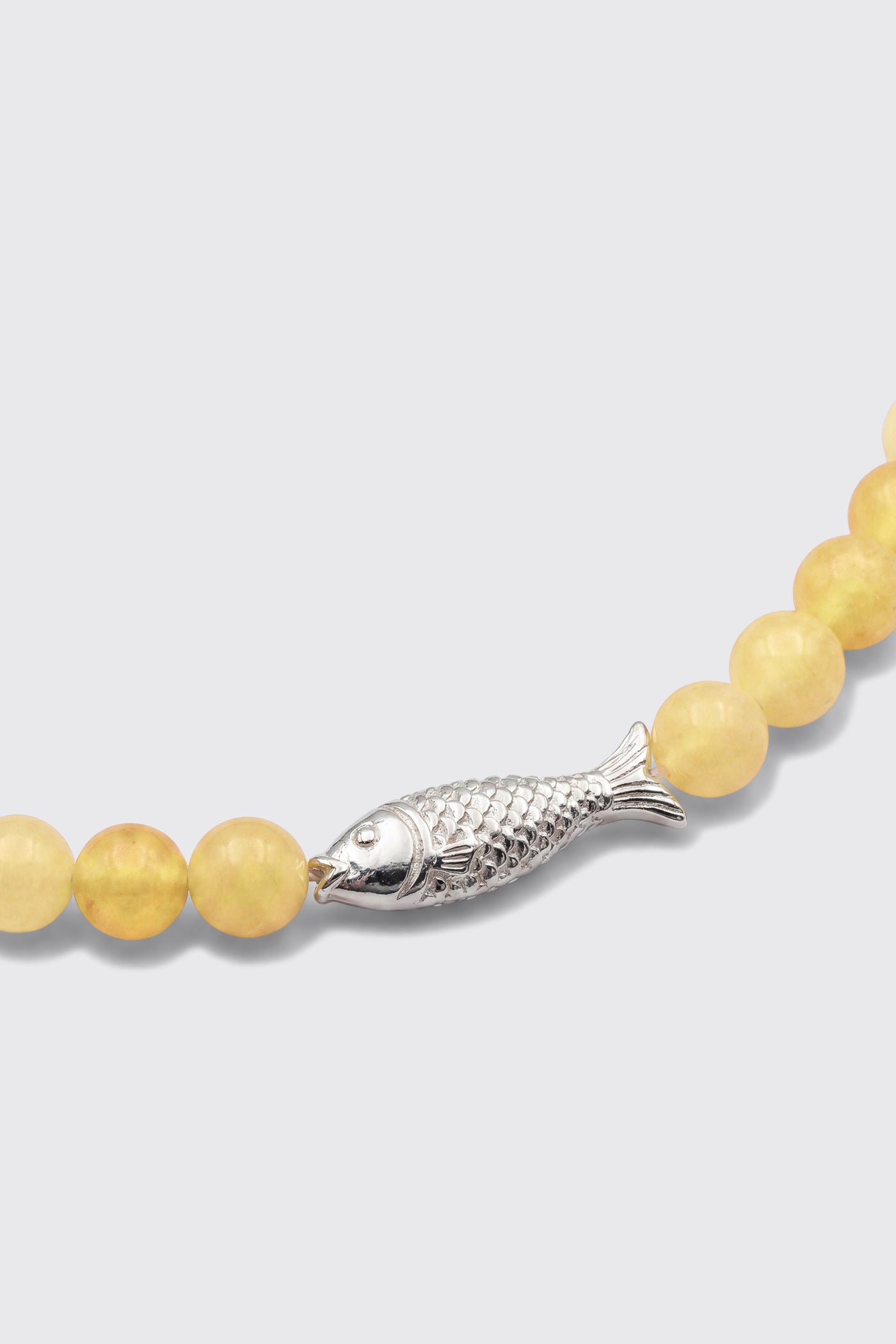 A close-up of the Amoura - Lemon bracelet, showcasing its beaded yellow stones and a silver fish-shaped charm.