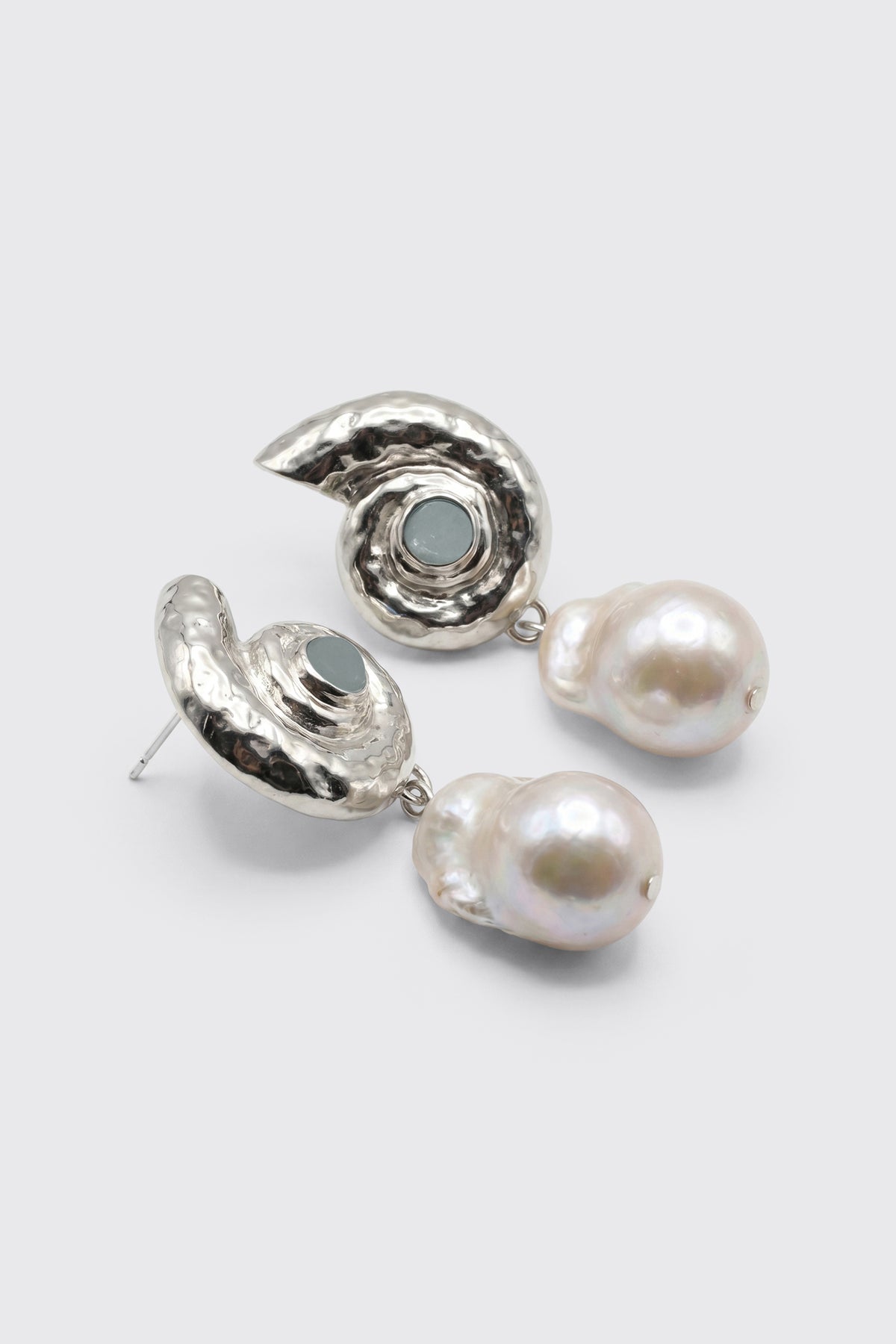 Introducing "Cali - Silver": Silver earrings shaped like seashells, each set with a small blue stone and complemented by large, irregular white pearls dangling below. Displayed on a plain light gray background.