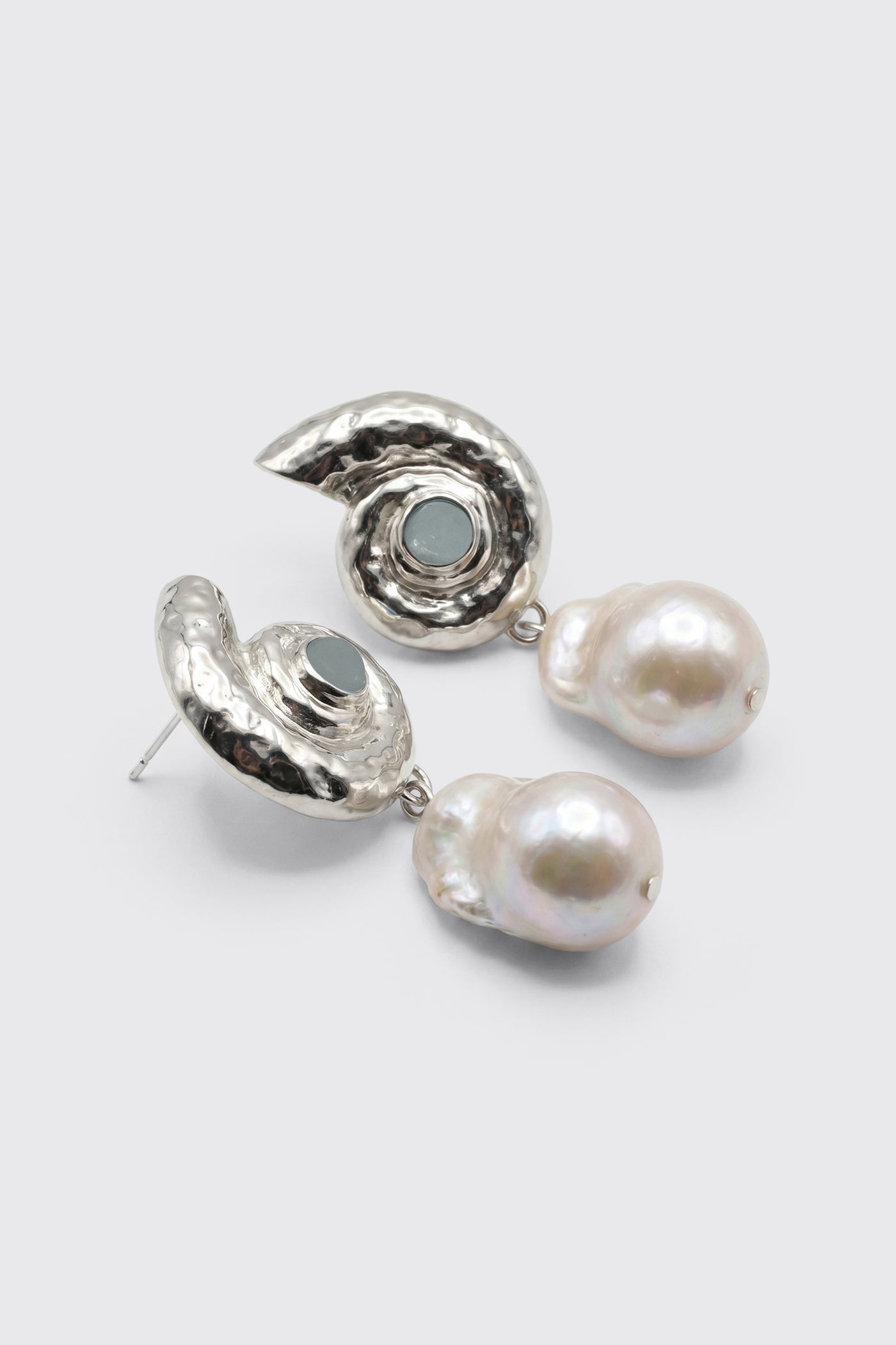 Introducing "Cali - Silver": Silver earrings shaped like seashells, each set with a small blue stone and complemented by large, irregular white pearls dangling below. Displayed on a plain light gray background.