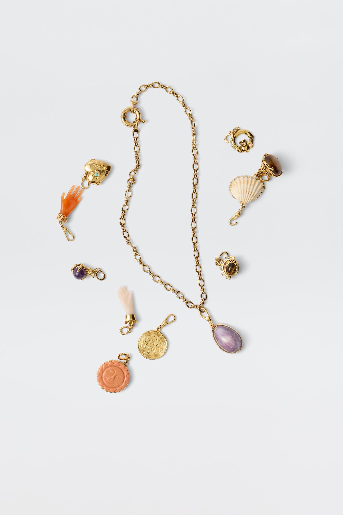 The Orsina - Gold necklace features gold plating and a mix of colorful pendants—purple stone, gold coins, orange hand, seashell, tassel, and more—artfully arranged on a white background.