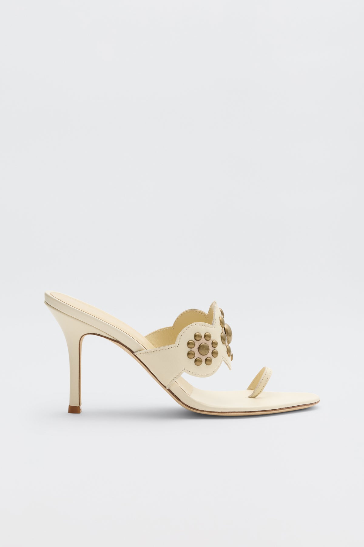 Introducing the Esmeray - Cream: a single cream-colored high heel mule sandal featuring decorative circular cutouts and gold studs on the strap, an open toe design, and a slender stiletto heel, showcased against a plain light background.