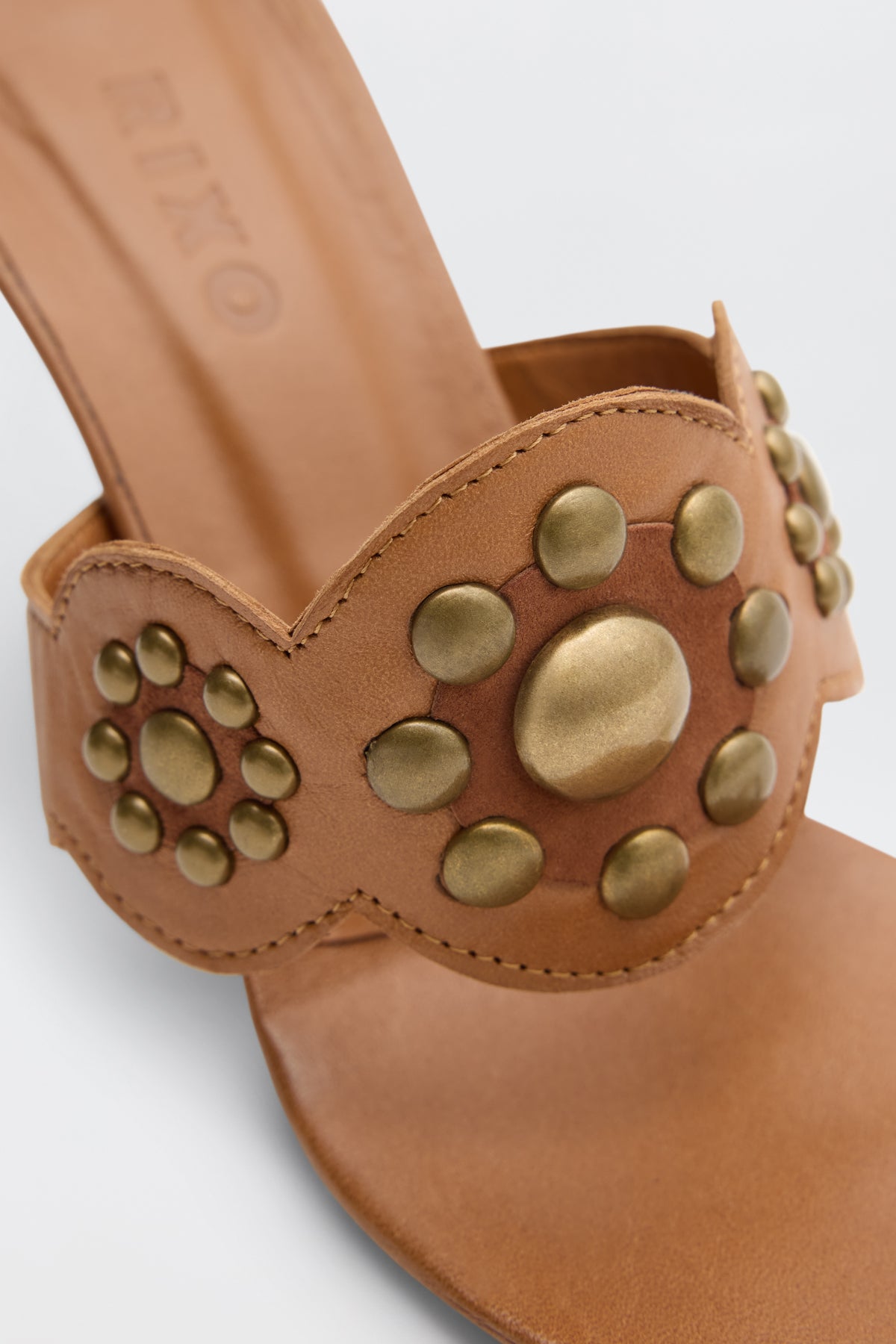 Close-up of Esmeray - Tan sandal in tan leather with decorative gold studs arranged in circular patterns on the strap, visible stitching, and a smooth finish.