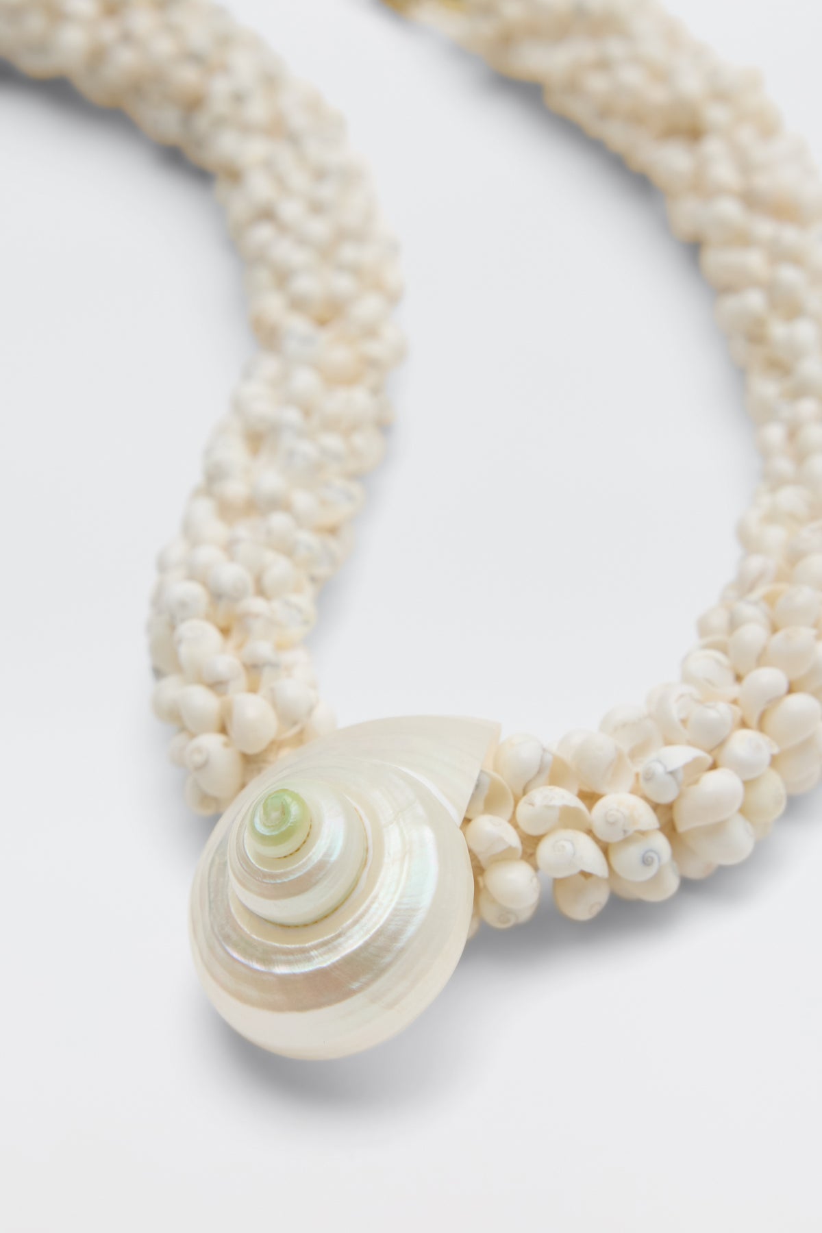 A close-up of the Imara - Pearl necklace, crafted from small white seashell beads woven together and showcasing a large spiral shell pendant.