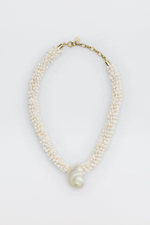 Imara - Pearl: A beaded necklace with small white beads, a large spiral seashell pendant, gold clasp, and adjustable chain, displayed on a white background.