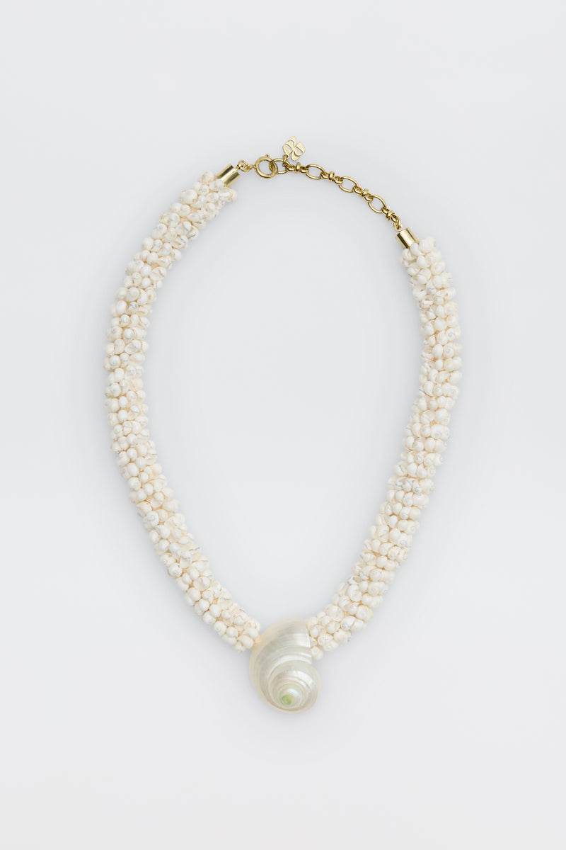Imara - Pearl: A beaded necklace with small white beads, a large spiral seashell pendant, gold clasp, and adjustable chain, displayed on a white background.