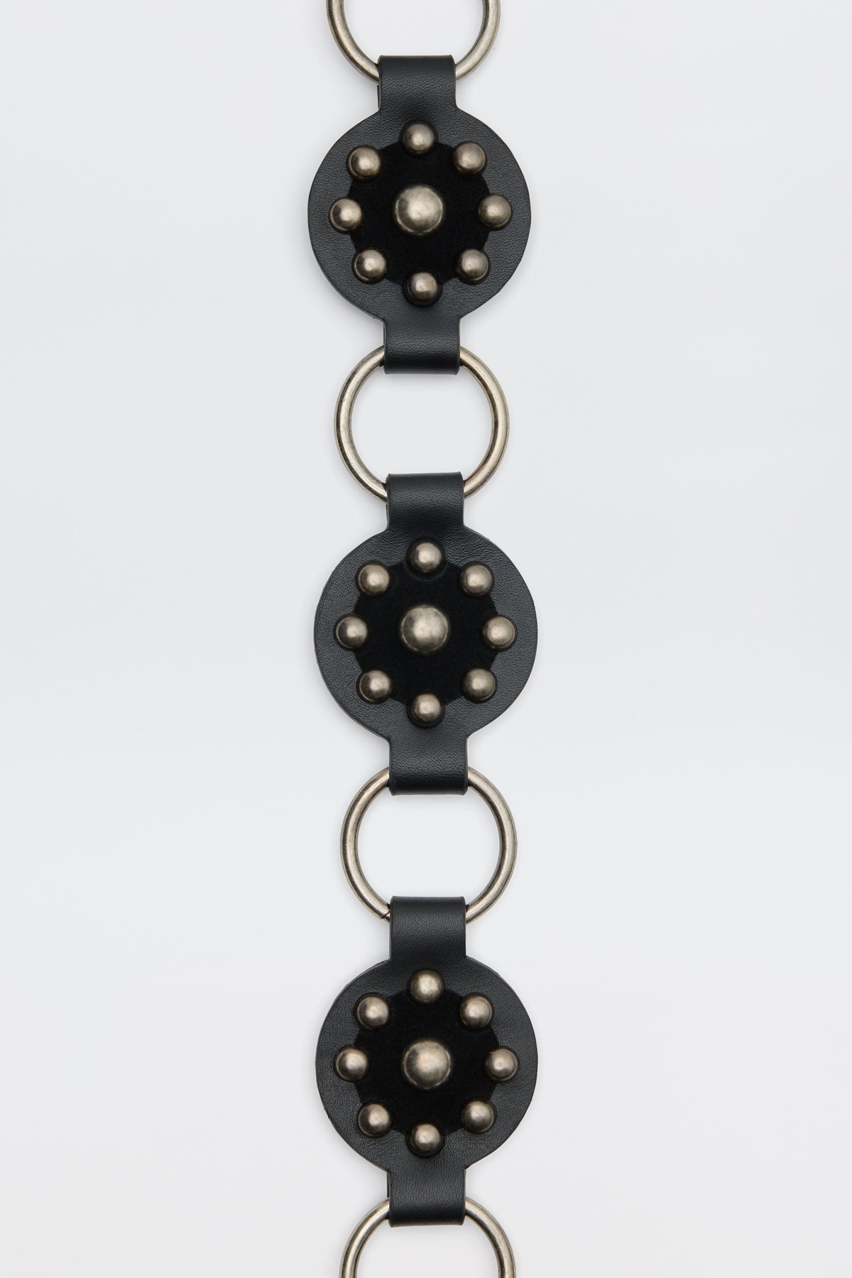 Kassy - Black: A vertical black leather strap featuring circular metal-studded accents connected by large silver rings, shown against a plain white background.