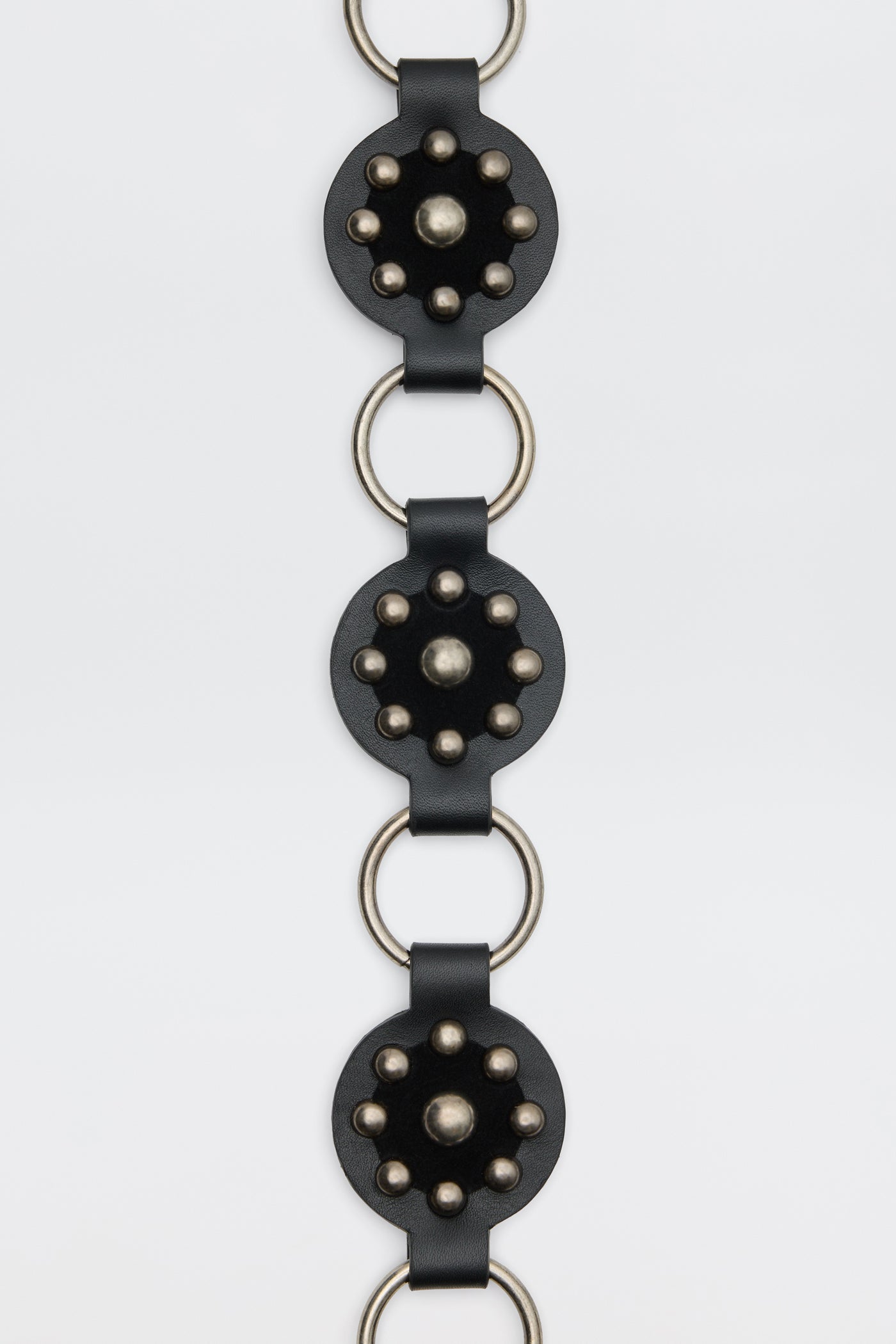 Kassy - Black: A vertical black leather strap featuring circular metal-studded accents connected by large silver rings, shown against a plain white background.