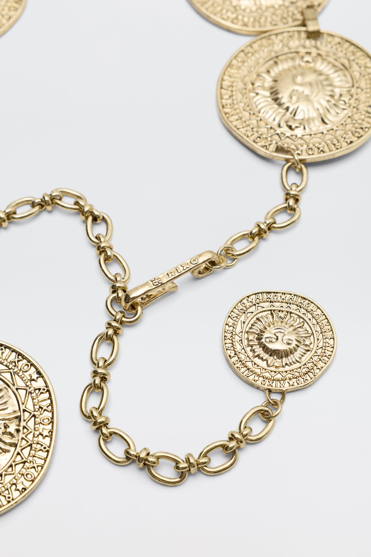 Close-up of the Leyla - Gold necklace, showcasing large round textured medallions with intricate designs and a decorative clasp, displayed on a light gray background.