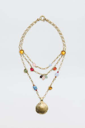 Lima - Gold necklace featuring three layered gold chains adorned with colorful beads, round yellow and green accents, and finished with a large gold seashell pendant, displayed on a plain white background.