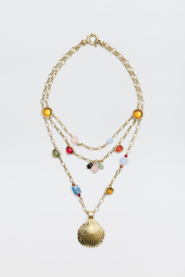 Lima - Gold necklace featuring three layered gold chains adorned with colorful beads, round yellow and green accents, and finished with a large gold seashell pendant, displayed on a plain white background.