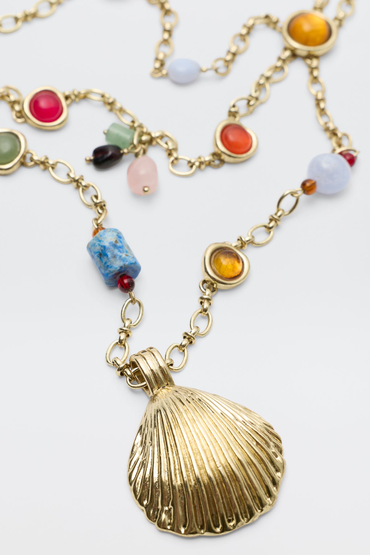 Introducing Lima - Gold: a necklace featuring a large gold seashell pendant adorned with colorful gemstones, all set on elegant gold-linked chains.