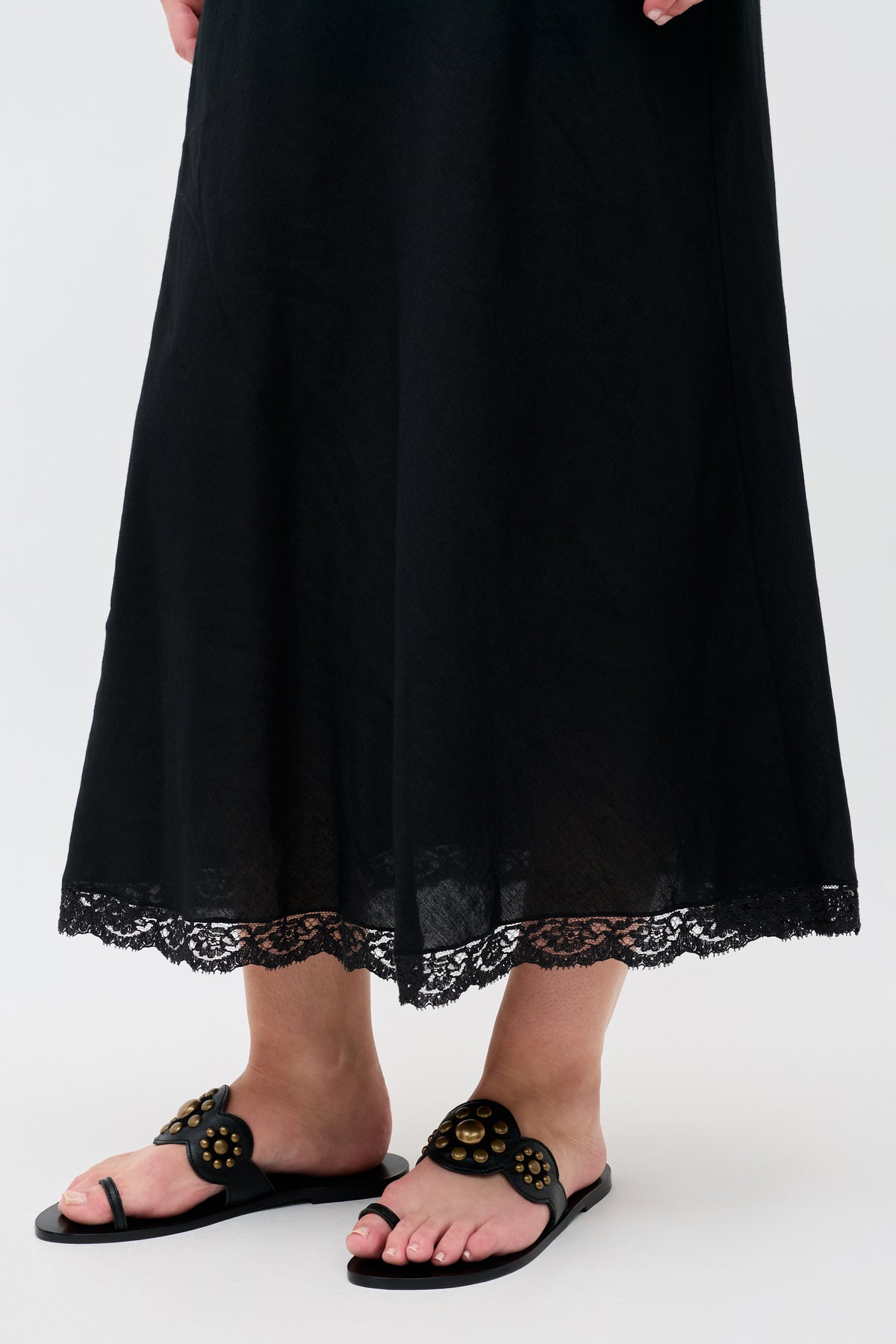 Wearing the Lucille - Black skirt with lace trim at the hem, this person stands in stylish black sandals against a plain light background.