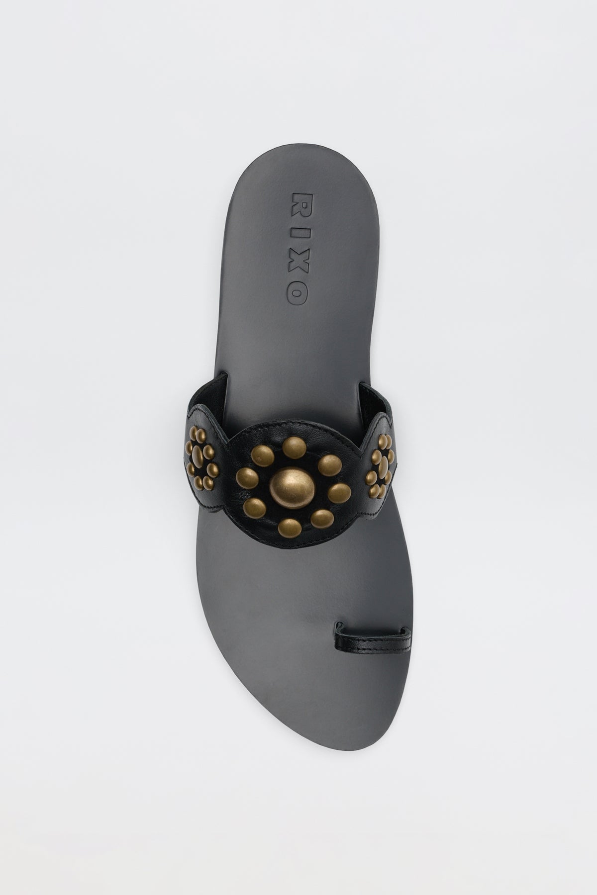 The Lucille - Black sandal features a wide strap adorned with large and small round gold studs, a loop for the big toe, and RIXO embossed on the insole.