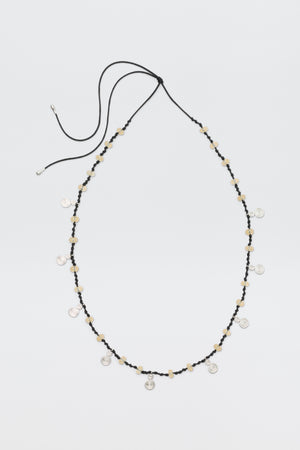 A long black cord necklace called "Mikah - Silver," featuring beige beads and small round silver charms evenly spaced, is displayed on a plain white background with the cord ends untied.