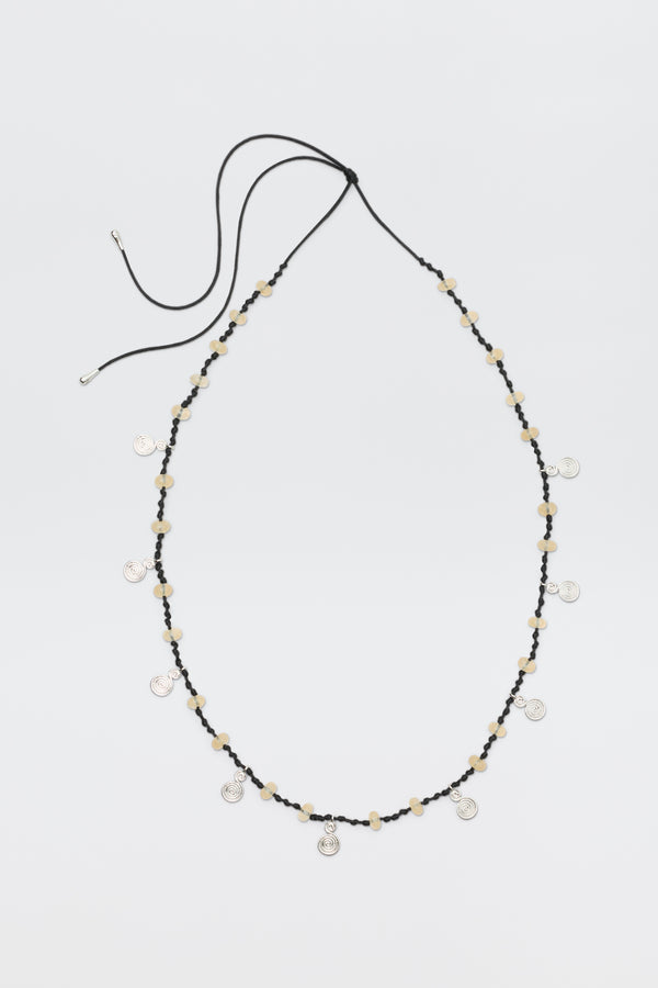A long black cord necklace called "Mikah - Silver," featuring beige beads and small round silver charms evenly spaced, is displayed on a plain white background with the cord ends untied.