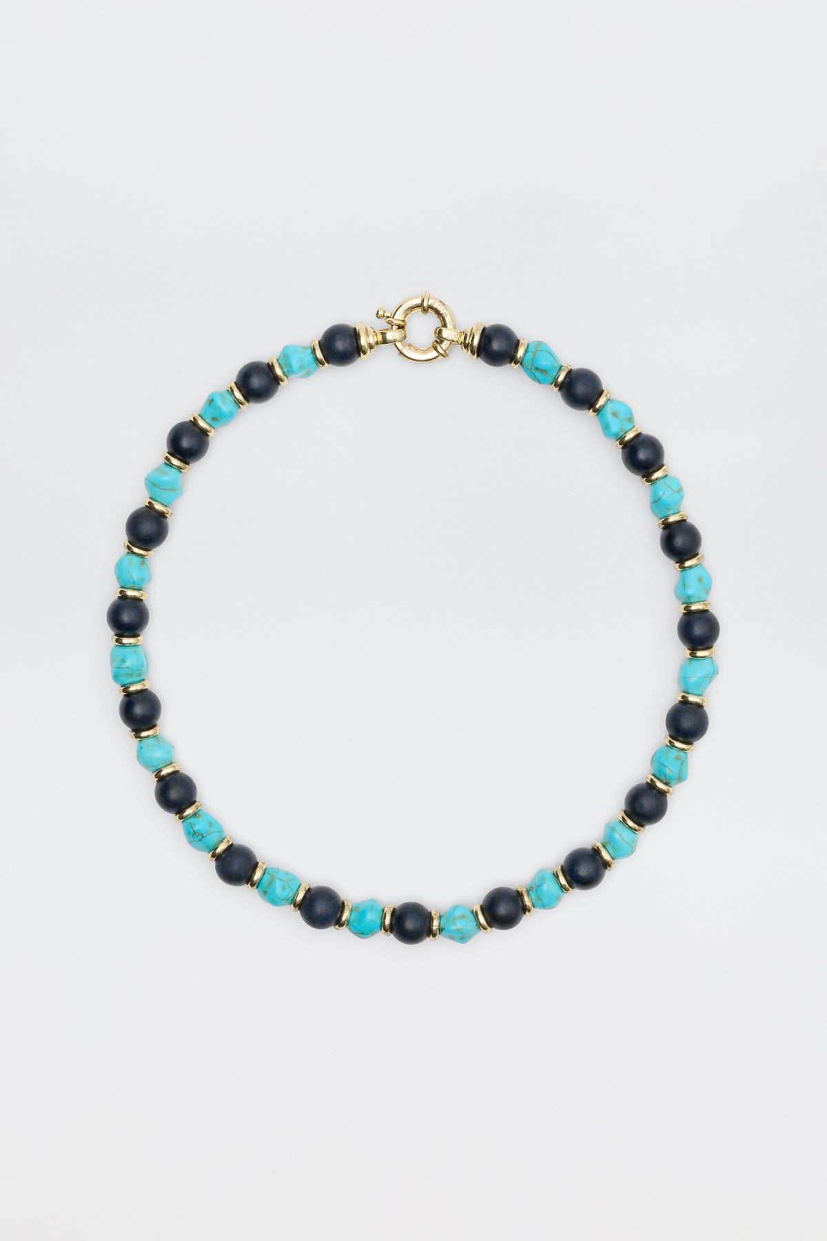 The "Palmara - Blue" necklace features alternating blue-green and dark blue round beads with gold spacers and a gold spring ring clasp, elegantly displayed against a plain light background.