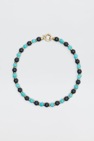 The "Palmara - Blue" necklace features alternating blue-green and dark blue round beads with gold spacers and a gold spring ring clasp, elegantly displayed against a plain light background.