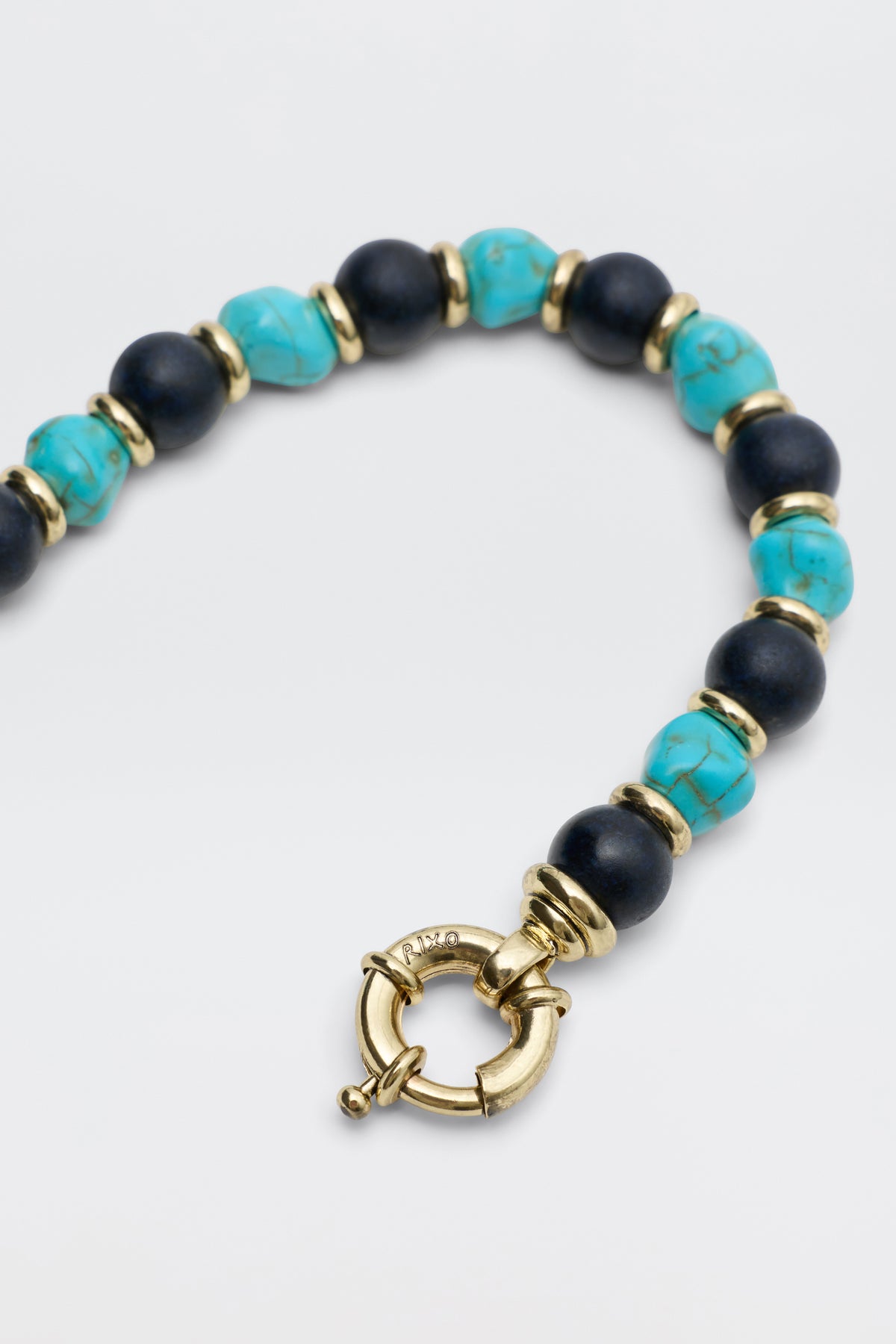 A close-up of the Palmara - Blue necklace shows alternating turquoise and black beads, separated by gold spacers, with a bold gold circular clasp at the center.
