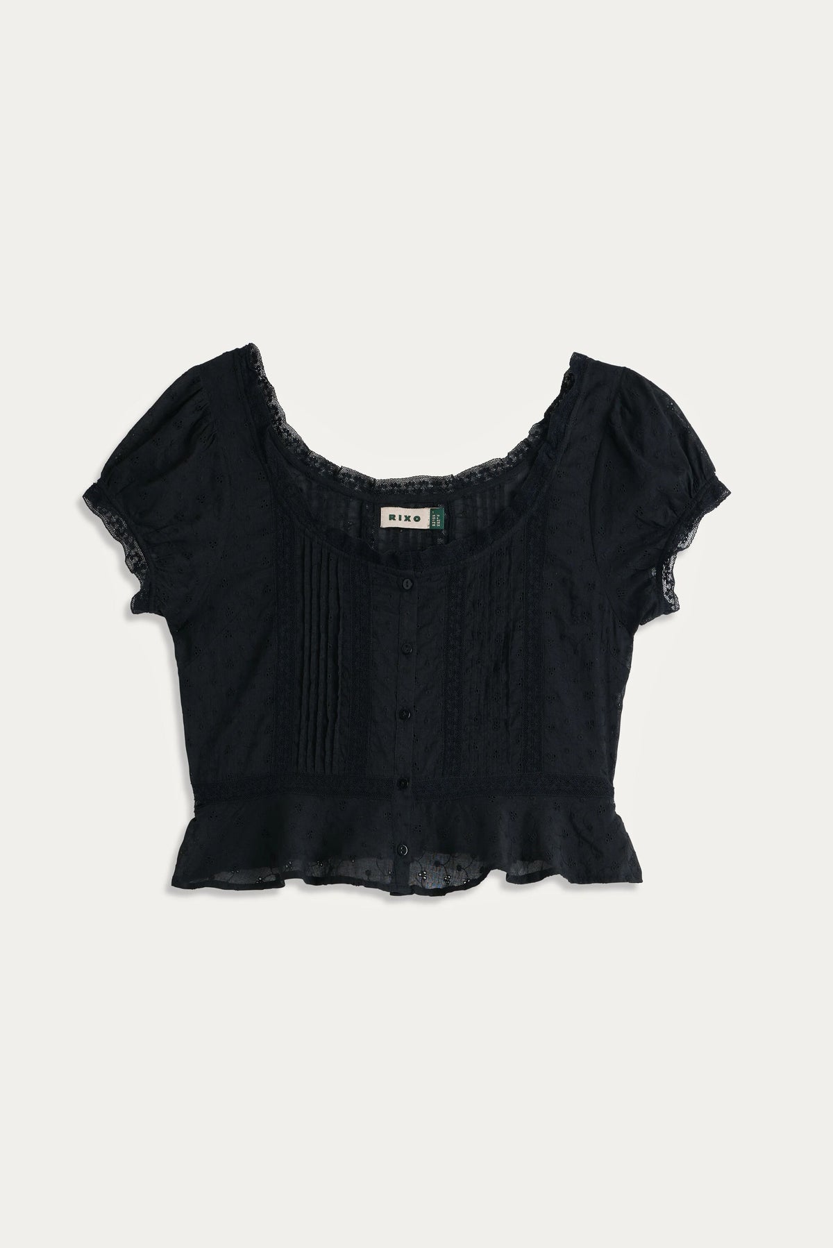 The Sandi - Black is a short-sleeved, button-up broderie anglaise cotton blouse with a scoop neckline, lace trim and inserts, pintuck front details, and a ruffled hem—perfect for effortless everyday style.