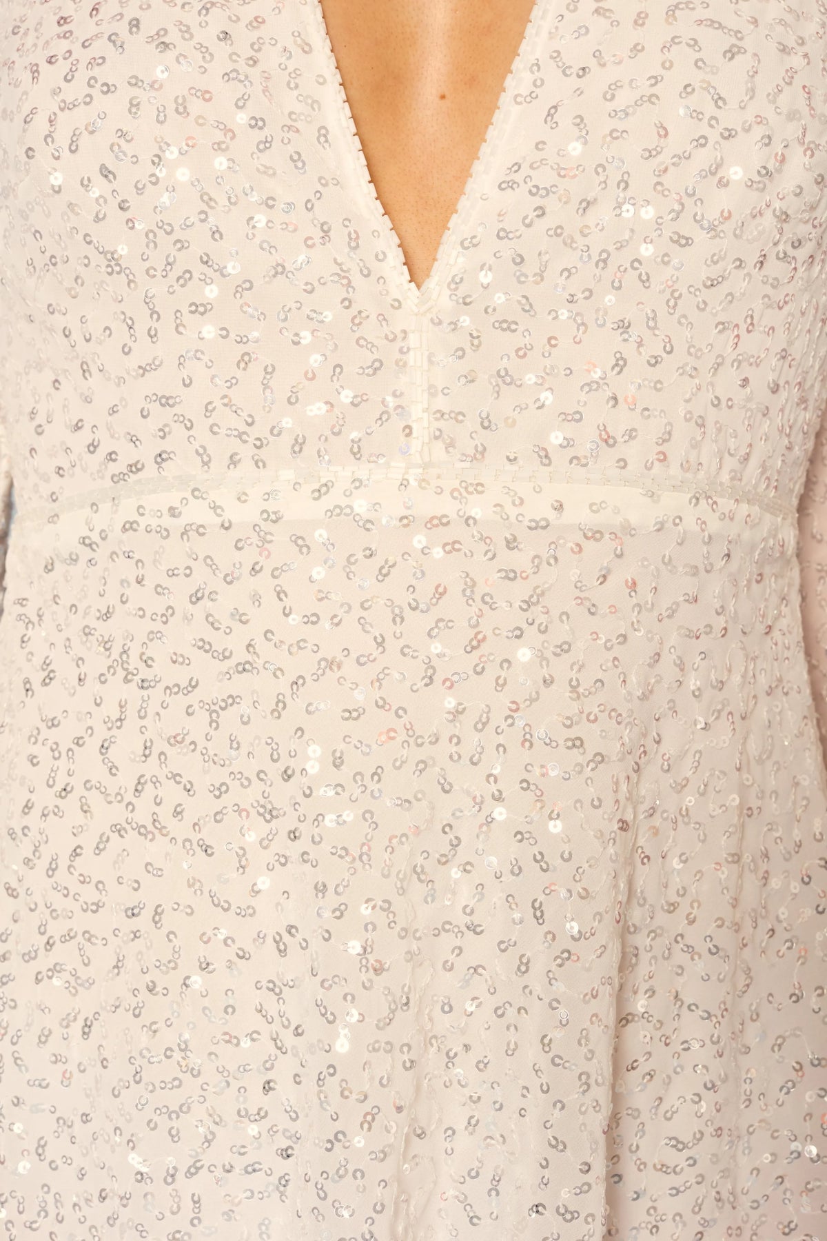 Close-up of the Sira - Squiggle Embellishment Ivory mini dress, featuring a cream-colored, V-neck design adorned with small, shimmering squiggle-shaped sequins in a scattered pattern. The fabric appears soft and slightly sheer, with a seam below the bust.