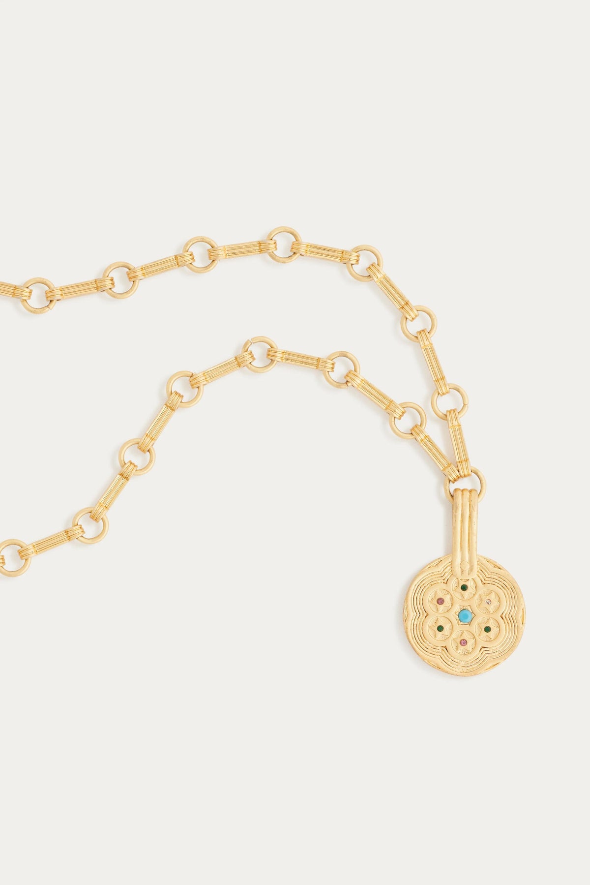 The Sol - Gold necklace features circular links and a round pendant with intricate patterns and a small blue gemstone at the center, shown against a plain white background.
